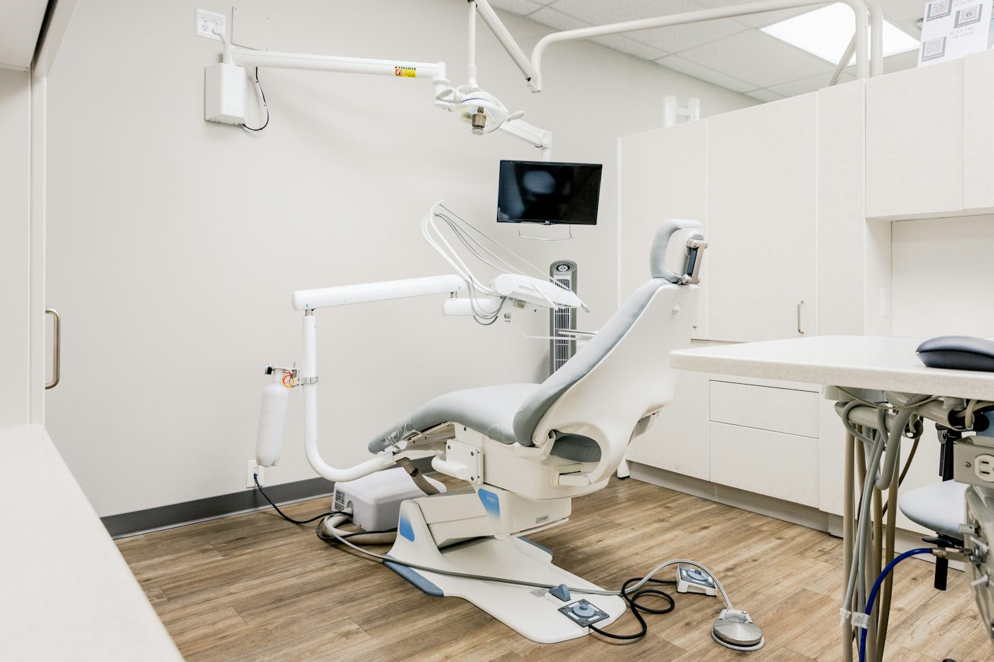 Bright treatment room with a gray dental chair and wood floor